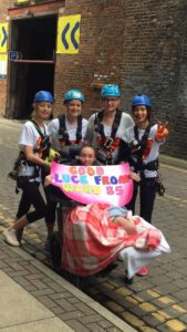 Rosie in a wheelchair with staff from Ward 85 dressed in harnesses and crash helmets for a charity abseil