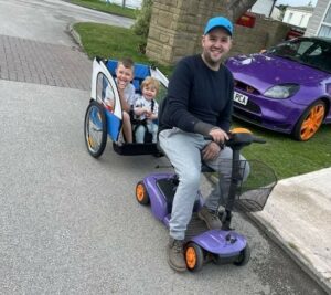 Kieran on a mobility scooter pulling his children in a wheeled trailer