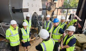 A group of people wearing hard hats and hi-vis jackets gathered around a large boiler
