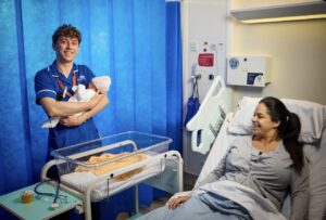 A male midwife holds a baby while the mum smiles