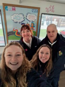 Group selfie of four of the NWCCODN team standing in front of a colorful care at home poster