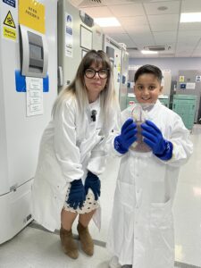 A boy wearing a lab coat holding a frozen unit of blood next to a woman wearing a lab coat. 