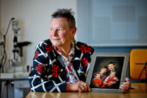 Photo of Helen Beaumont sat at a table holding a framed family photo of her late husband Clive and their three children