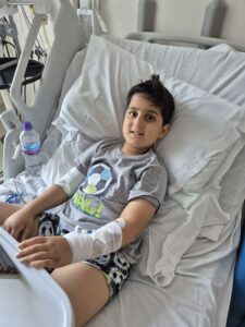 Boy sat in a hospital bed smiling to camera.