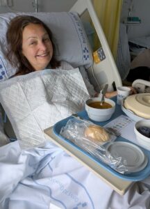 Woman sat in hospital bed eating meal.