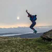 Woman jumping on a hillside in front of a sunset.