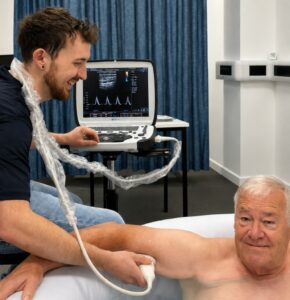 Man sat in bath while member of staff monitors him. 
