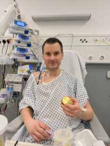 Man in hospital gown sat up in bed eating an apple.
