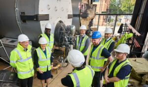 A group of people wearing hard hats and hi-vis jackets gathered around a large boiler