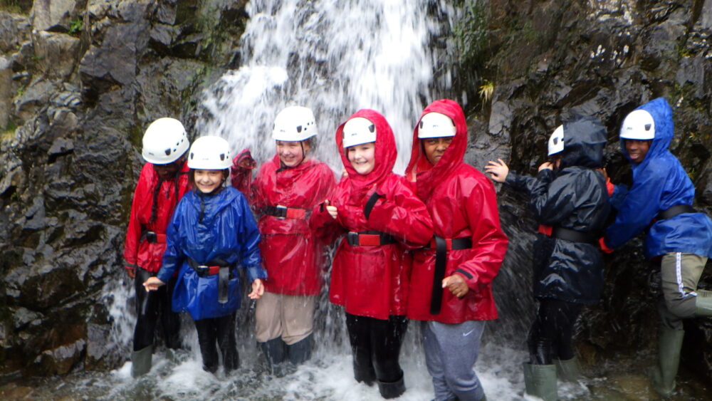 Group of children stood under a waterfall wearing helmets