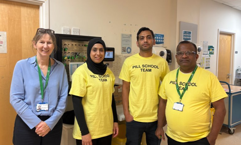 Group of four people stood in hospital. Three are wearing yellow Pill School Team tshirts.