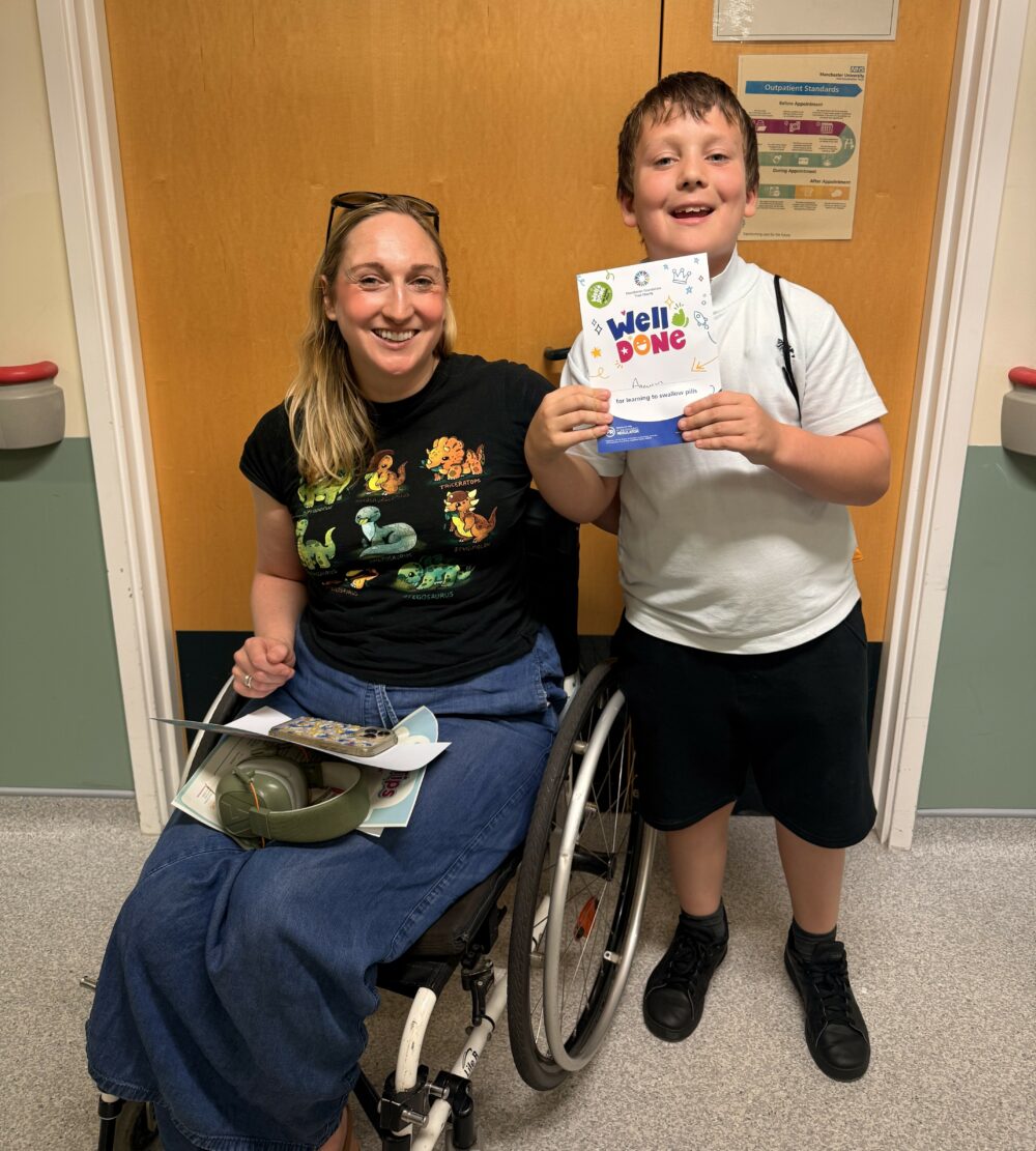 A child holding a certificate stood next to a woman in a wheelchair.